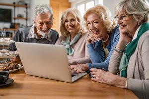 Group of happy mature people surfing the Internet on laptop at h
