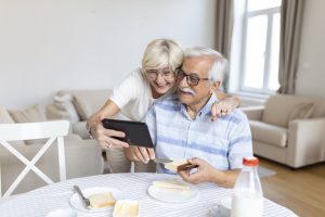 Happy old family couple talking with grandchildren using tablet , surprised excited senior woman looking at tablet waving and smiling.